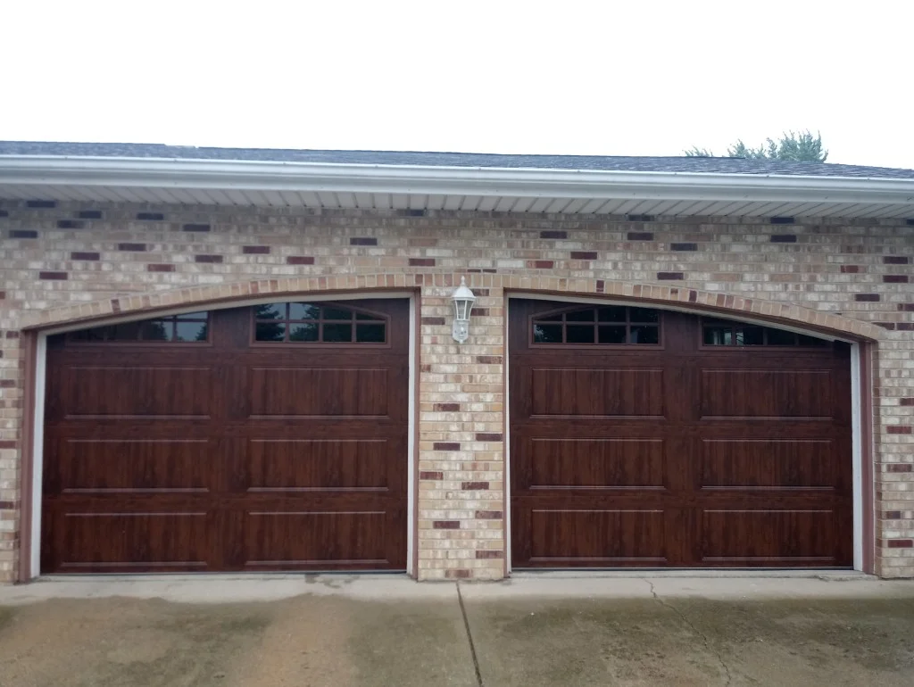 Beautiful dark wood-grain garage doors with arched windows on brick home